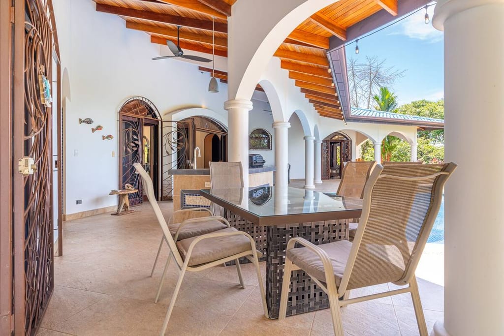 Covered outdoor dining table beside the pool under the villa's arches