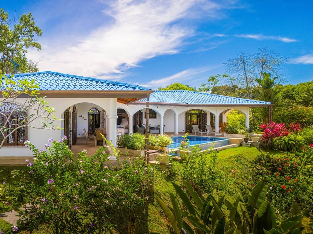 Casa Rosa Blanca seen across its gardens with the pool and flowering plants in the foreground