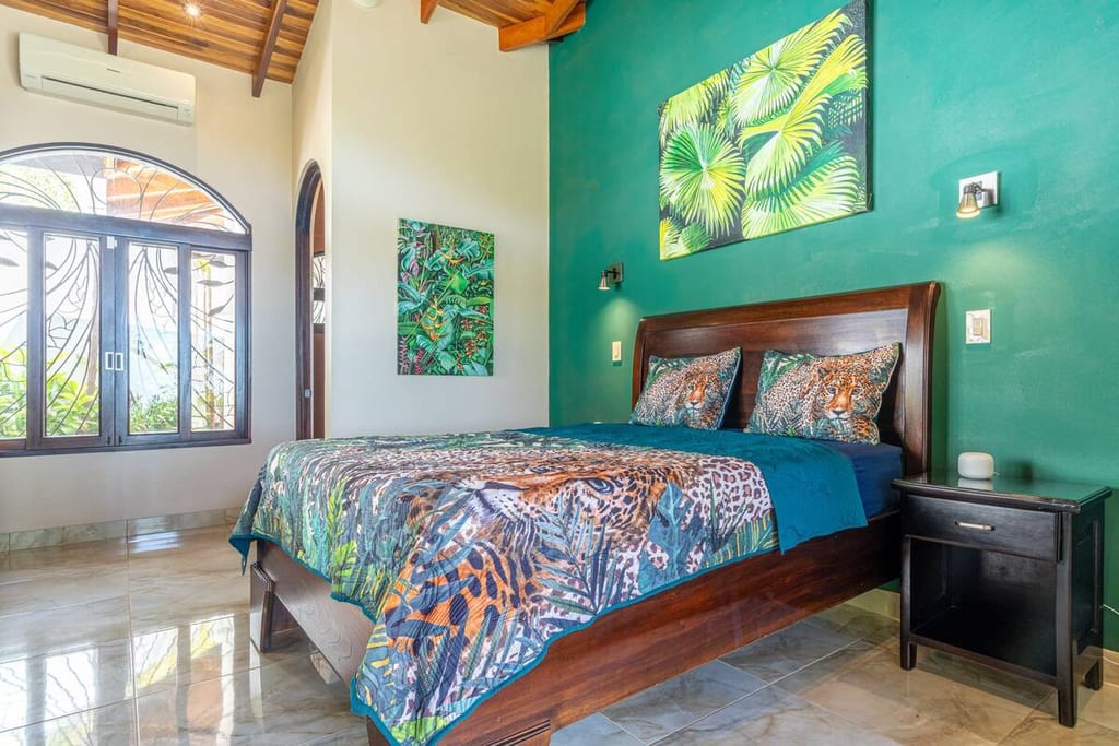 Jungle Room guest bedroom with queen bed and green accent wall with tropical artwork
