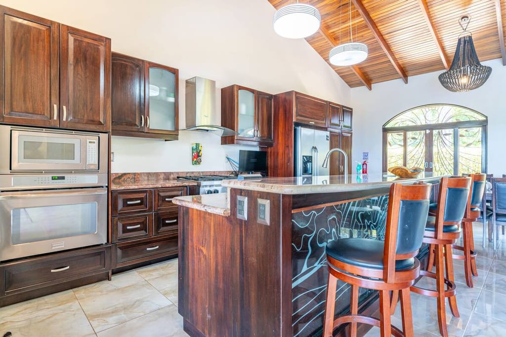 Full kitchen with hardwood cabinetry, island and bar seating at Casa Rosa Blanca
