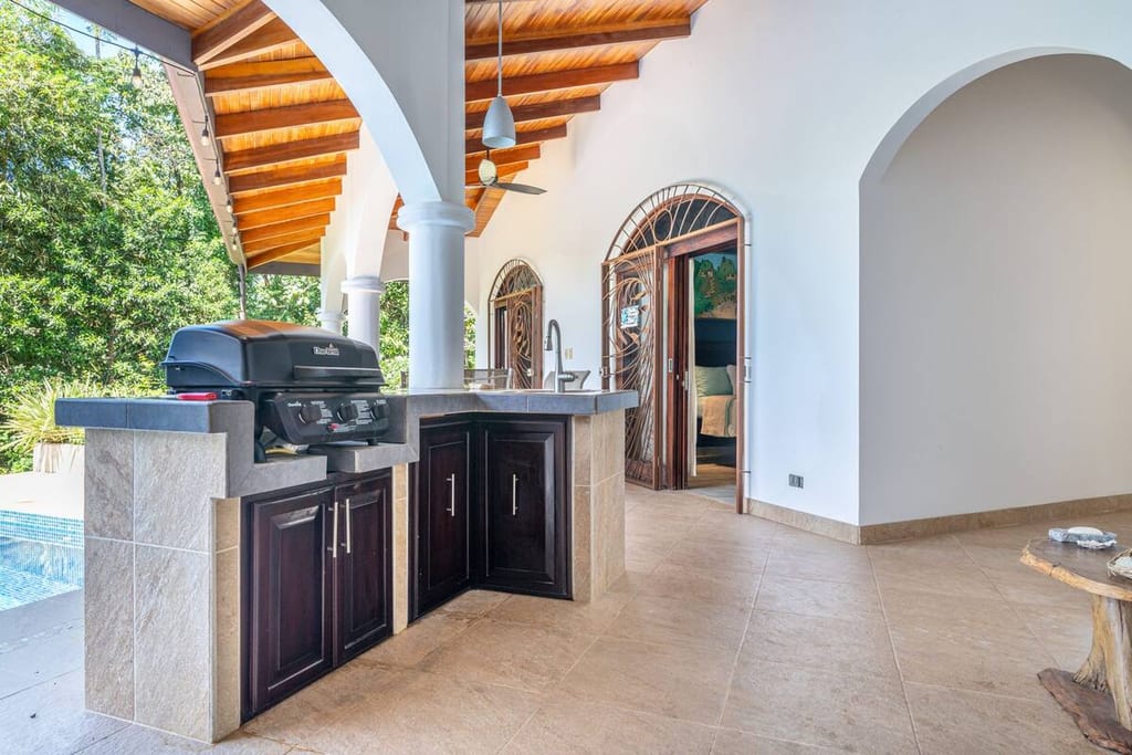 Covered outdoor kitchen with gas barbecue and preparation counter beside the pool