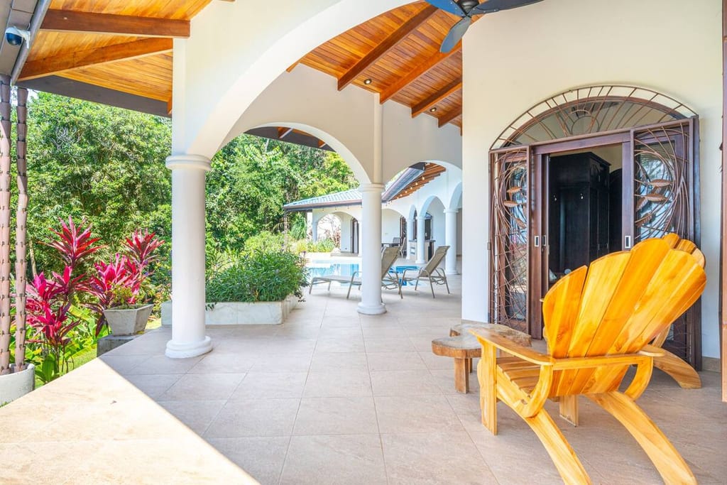 Covered terrace with hardwood chairs running the length of the villa toward the pool